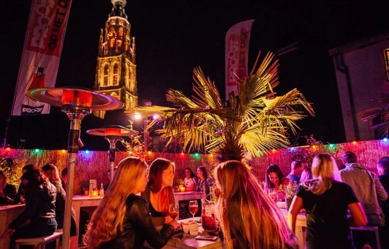 Borrelende mensen bij avond op het dakterras van Proost met uitzicht op de Grote Kerk Breda