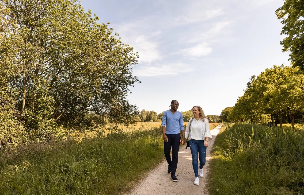 A couple walking down a sandy path in the Markdal, surrounded by trees.