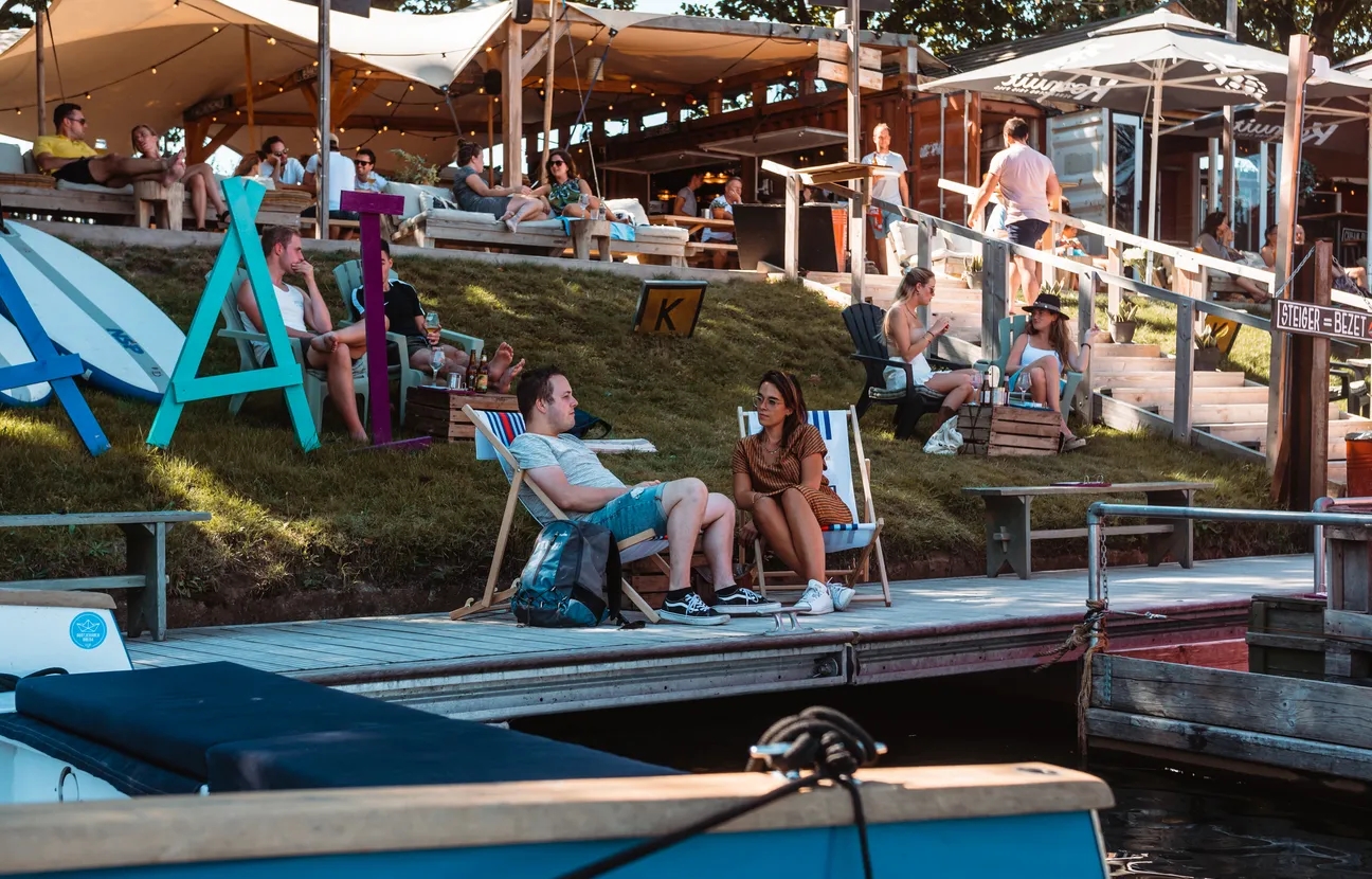 mensen op terras aan de waterkant zittend in strandstoelen